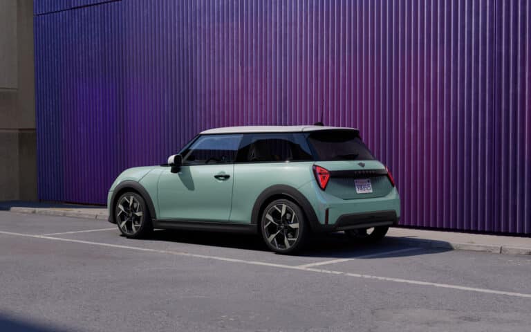 Mintgrüner Mini Cooper mit weißem Dach auf Parkplatz vor lila Wand.