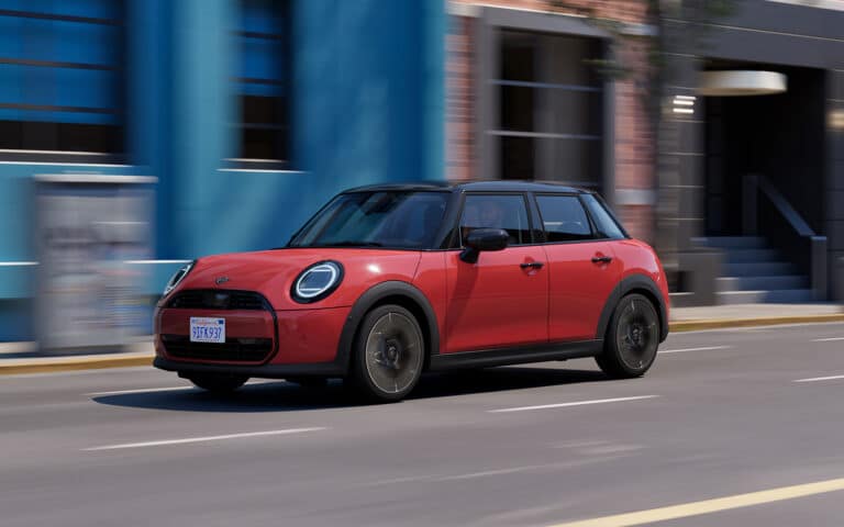 Roter Mini mit schwarzem Dach fährt durch Straße in urbaner Umgebung.