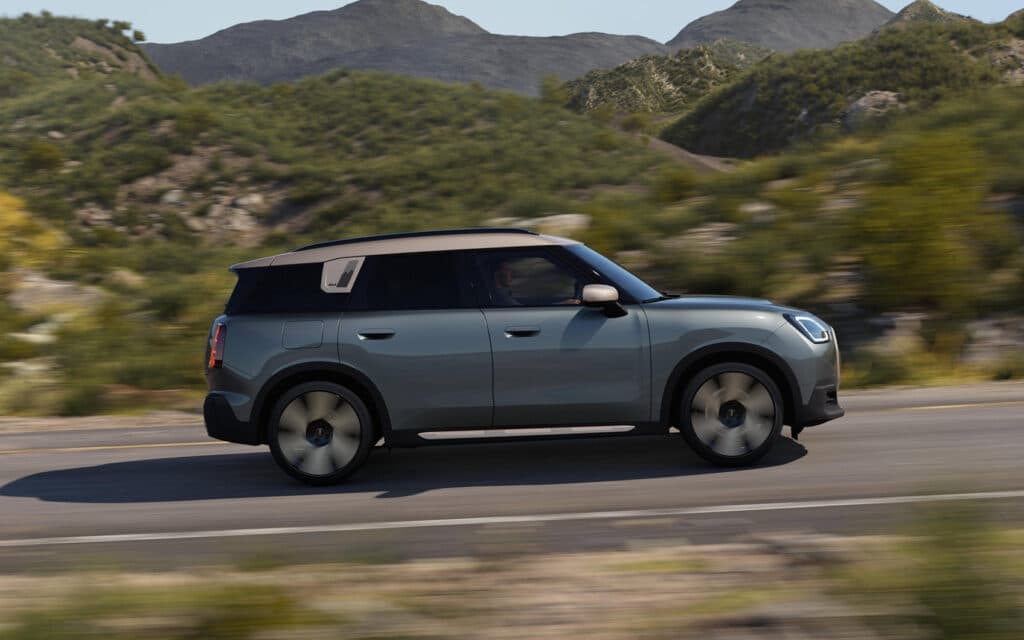 Alt-Text: Grauer Mini SUV fährt auf Landstraße durch hügelige Landschaft.