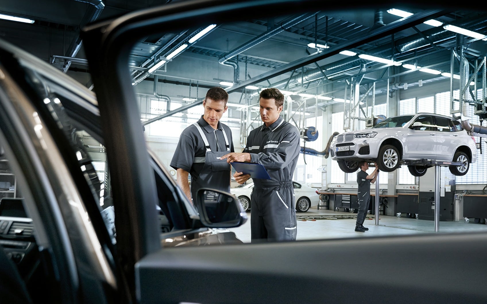 BMW Servicemitarbeiter prüfen Fahrzeug in heller Werkstatt, BMW X3 auf Hebebühne im Hintergrund