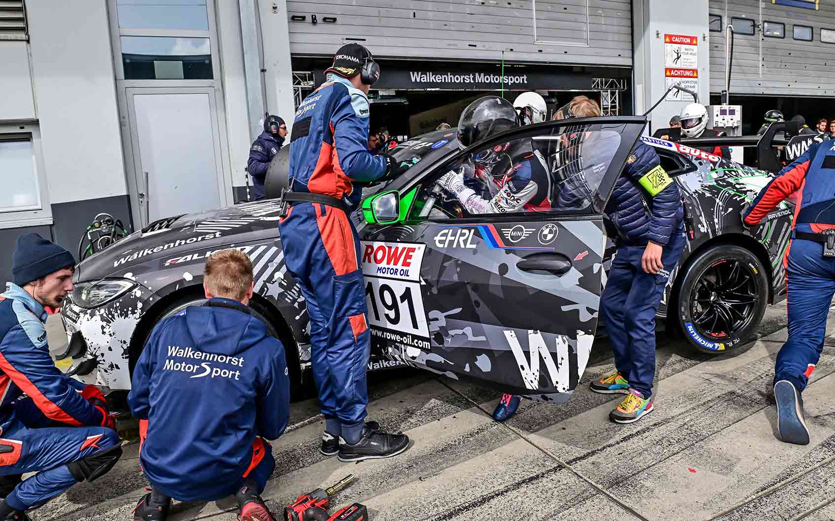 BMW Motorsport Mechaniker in blau-roter Arbeitskleidung arbeiten an einem Rennfahrzeug.