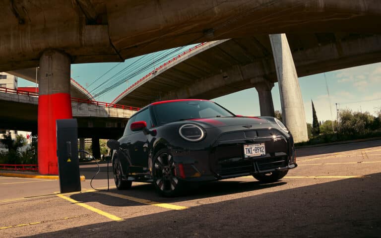 MINI John Cooper Works Electric in der Farbe Schwarz mit roten Sport Stripes angeschlossen an einer Ladesäule in einem Parkhaus