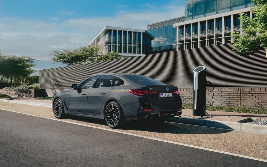 Grauer BMW i4 lädt an E-Ladesäule in urbaner Umgebung mit moderner Büroarchitektur.