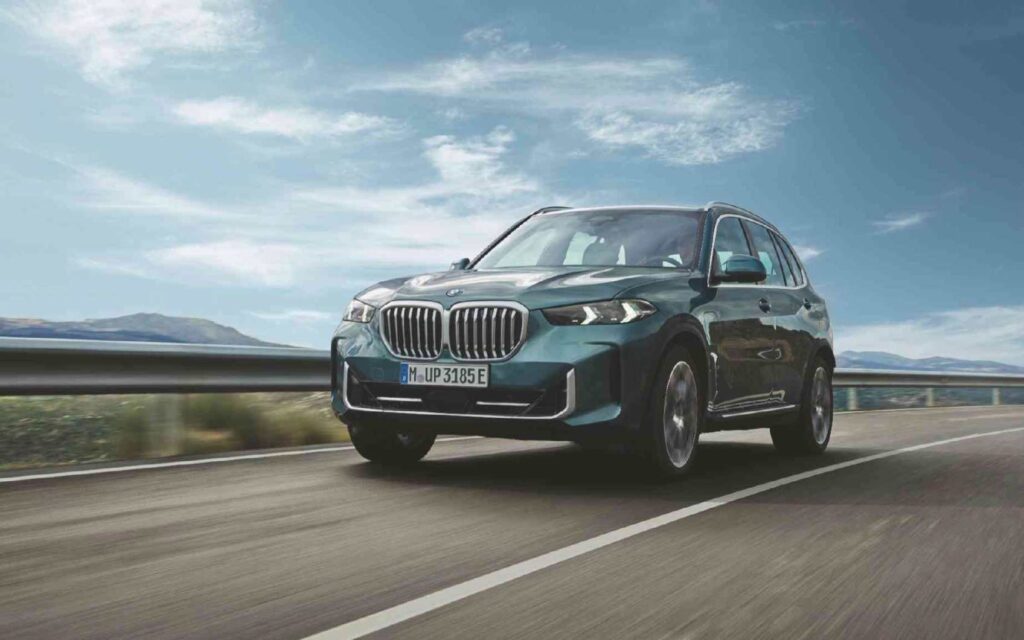 fahrender grüner BMW X5 auf LAndstraße mit blauem Himmel und Berglandschaft