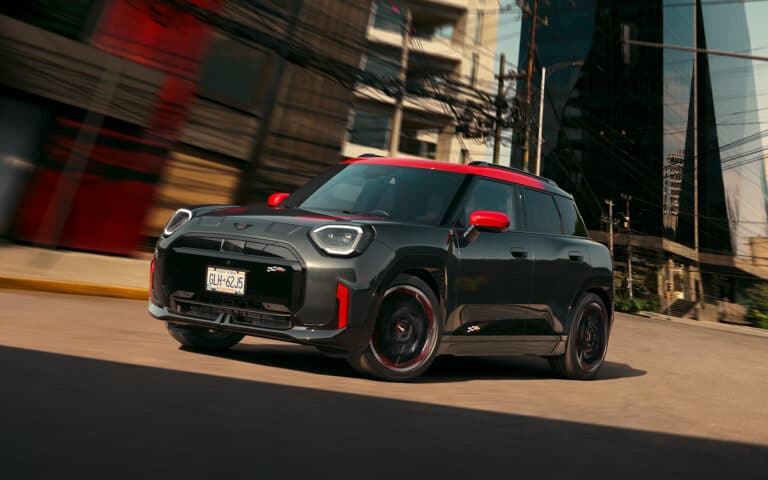 Profil und Frontansicht eines MINI John Cooper Works Aceman in der Farbe Schwarz mit roten Sport Stripes fahrend auf einer Straße