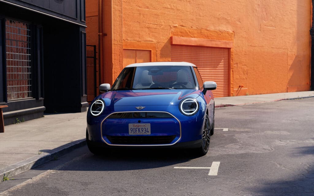Blauer Mini Cooper Electric mit LED-Tagfahrlicht vor orangefarbener Wand geparkt