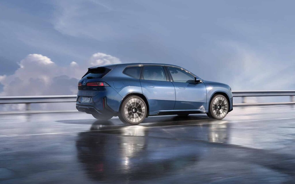 Seitenansicht eines blauen BMW iX3 auf nasser Straße bei blauem Himmel