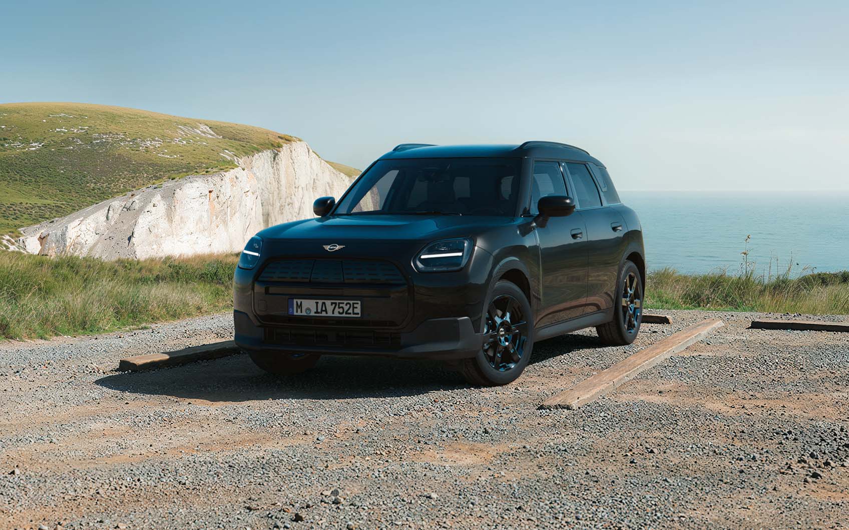 MINI Countryman Electric Blackyard parkend auf einem Schotterplatz vor Küstenlandschaft mit Klippen und Meer.