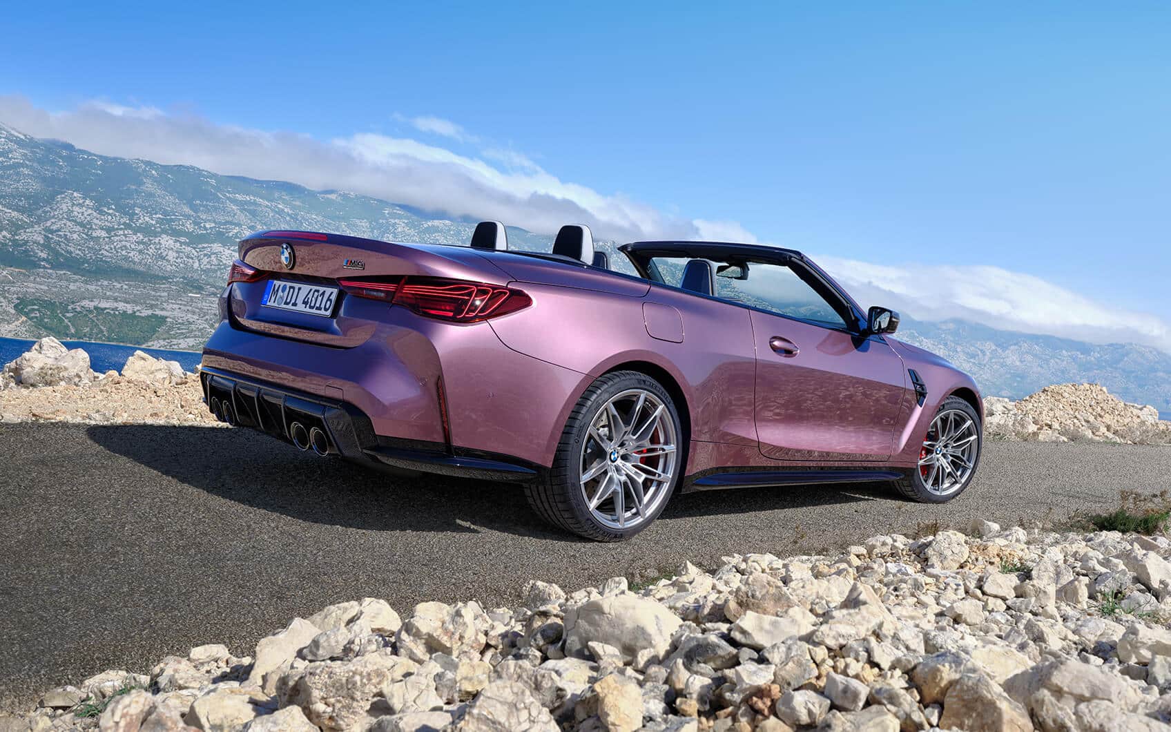 Rosafarbenes BMW M4 Competition Cabrio in Heck-Seitenansicht an Küstenstraße