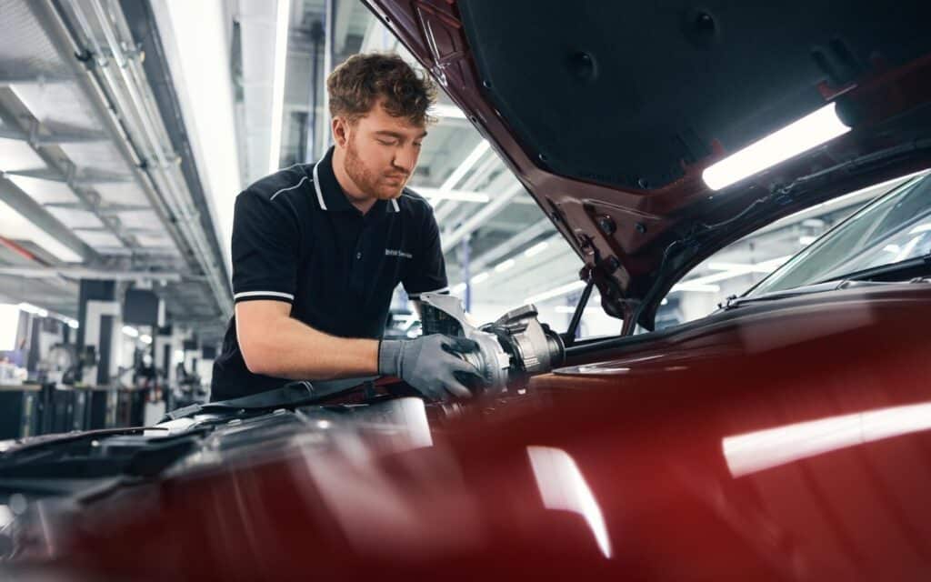 BMW Servicemitarbeiter arbeitet am Motorraum eines roten BMW in der Werkstatt.