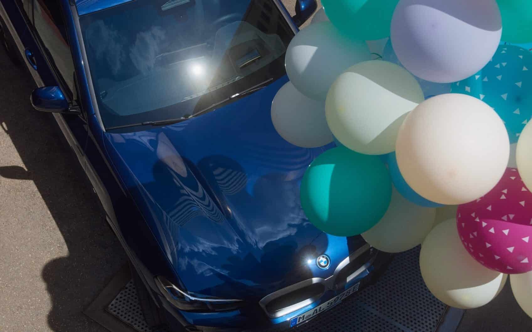 Blauer BMW von oben mit bunten Luftballons über der Motorhaube.