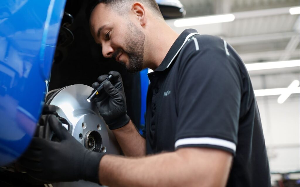 BMW Servicemitarbeiter prüft die Bremsscheibe eines blauen BMW.
